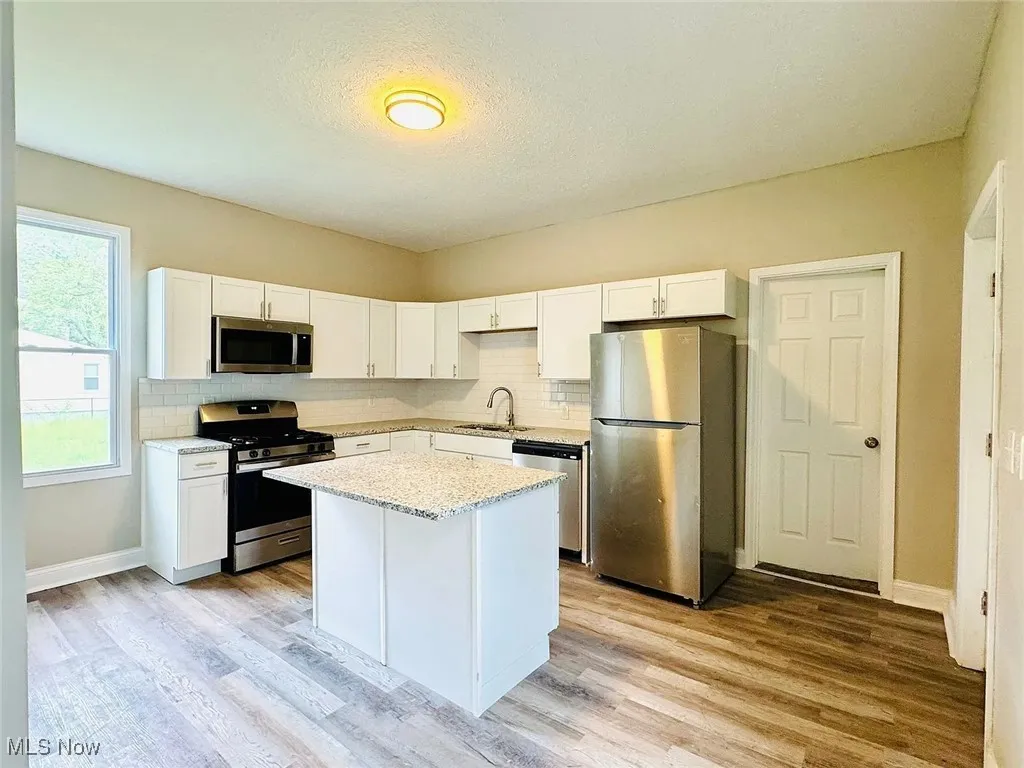 Kitchen with stainless steel appliances, a sink, decorative backsplash, light wood-style floors, and a textured ceiling