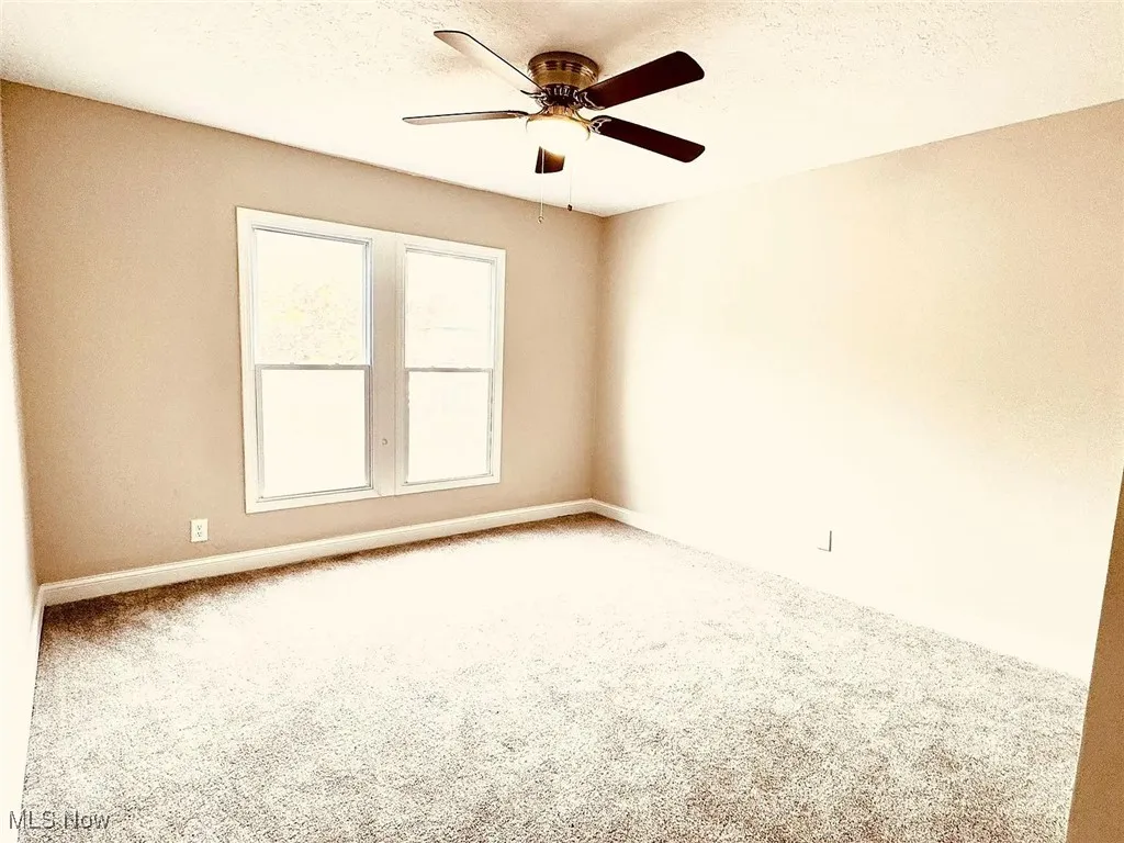 Empty room with carpet flooring, ceiling fan, baseboards, and a textured ceiling