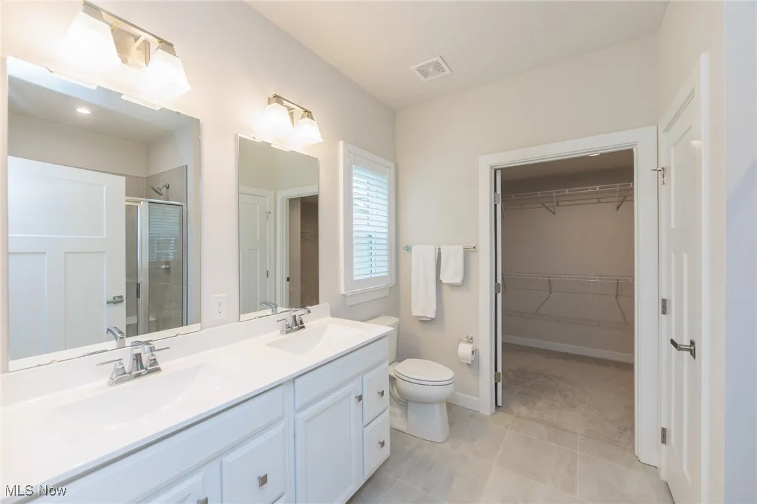 Bathroom featuring a stall shower, double vanity, a walk in closet,commode, and tile floor