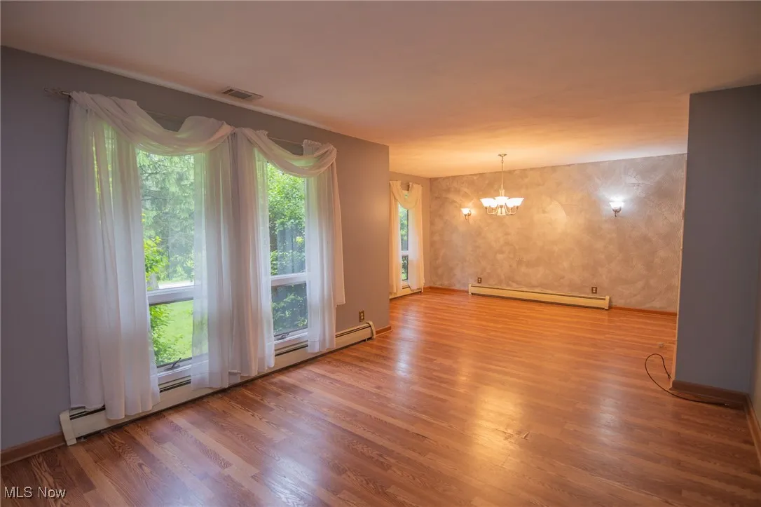 Spare room with baseboard heating, a chandelier, and wood finished floors