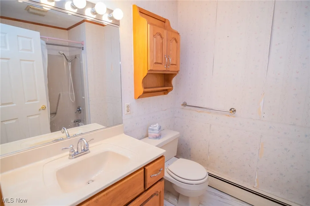 Bathroom with baseboard heating, vanity, toilet, wallpapered walls, and bathtub / shower combination