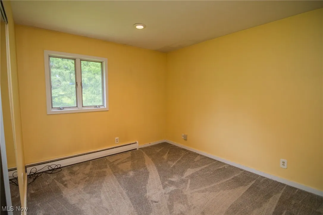 Empty room featuring dark carpet, a baseboard heating unit, baseboards, and recessed lighting