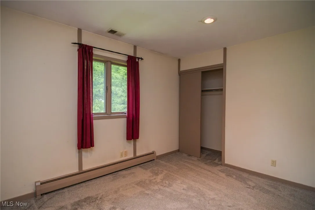 Unfurnished bedroom featuring a baseboard radiator, light colored carpet, a closet, and baseboards