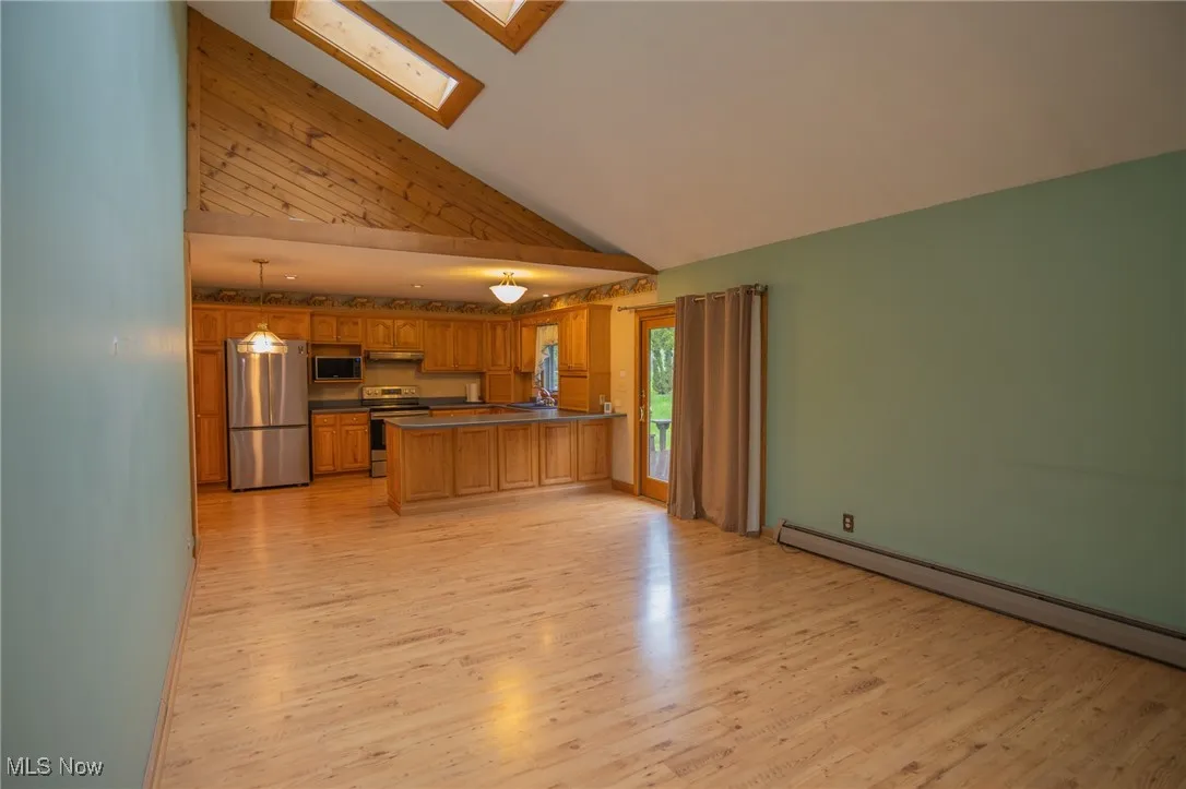Kitchen featuring stainless steel appliances, a skylight, a baseboard heating unit, a peninsula, and high vaulted ceiling