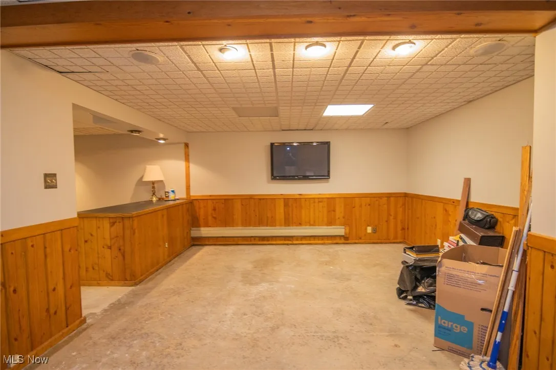 Finished below grade area featuring wainscoting, wooden walls, and a baseboard radiator