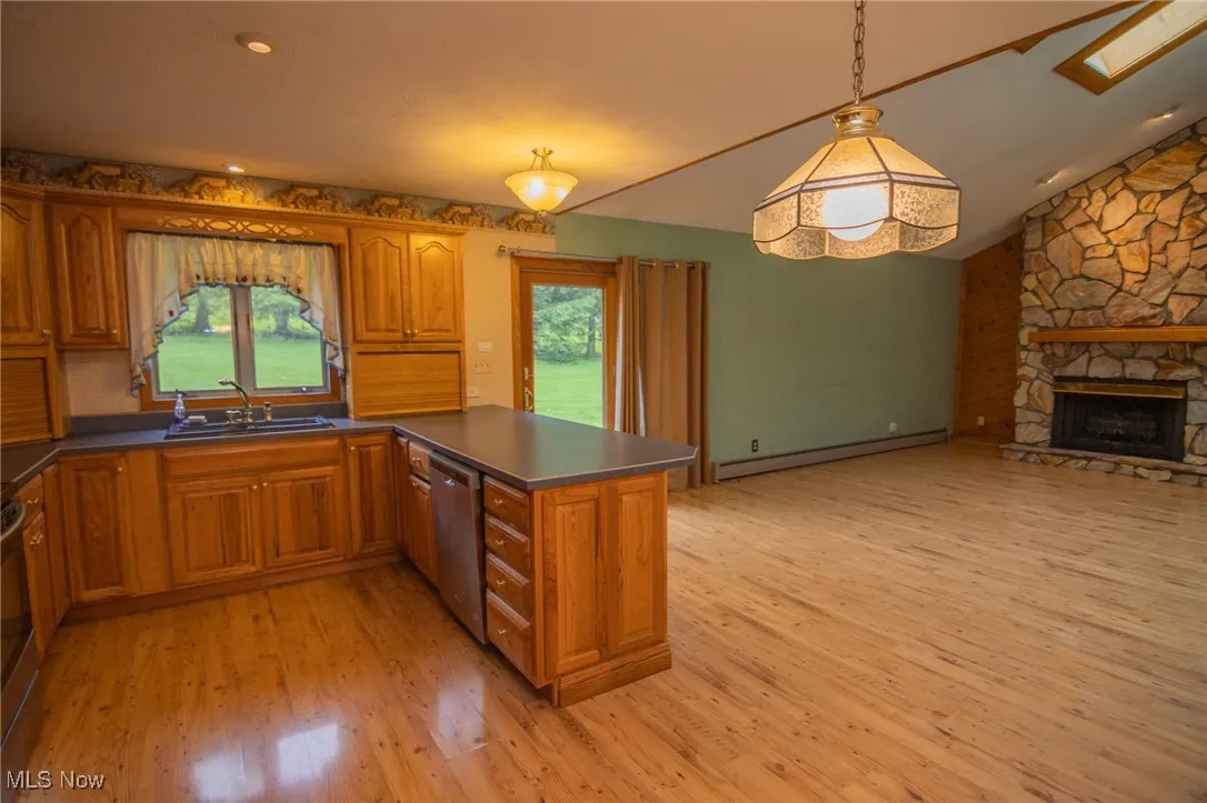 Kitchen with a sink, stainless steel dishwasher, baseboard heating, brown cabinetry, and vaulted ceiling