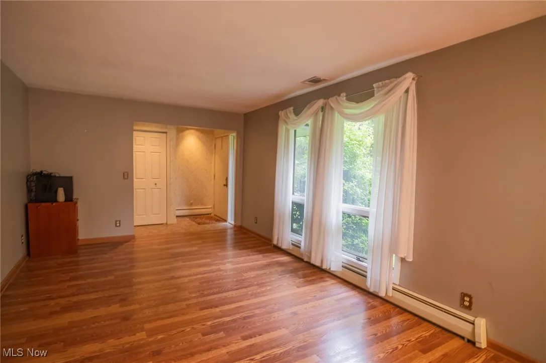 Empty room featuring wood finished floors, a baseboard radiator, and baseboards