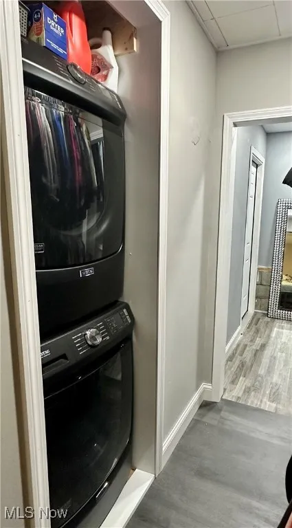 Laundry room with stacked washing machine and dryer, wood finished floors, and baseboards
