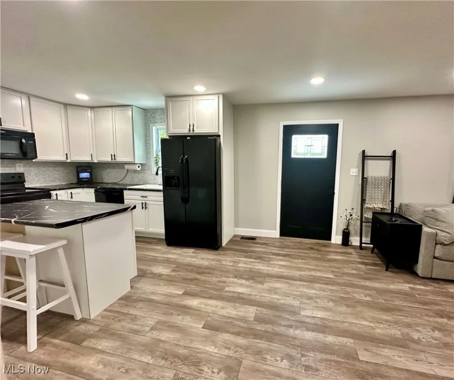 Kitchen featuring black appliances, white cabinets, light wood finished floors, recessed lighting, and dark countertops