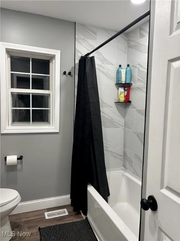Full bathroom featuring shower / tub combo with curtain, toilet, wood finished floors, and baseboards