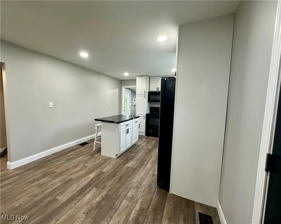 Kitchen featuring black appliances, white cabinetry, dark countertops, dark wood-type flooring, and recessed lighting