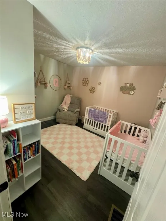 Bedroom with a textured ceiling, wood finished floors, and a nursery area