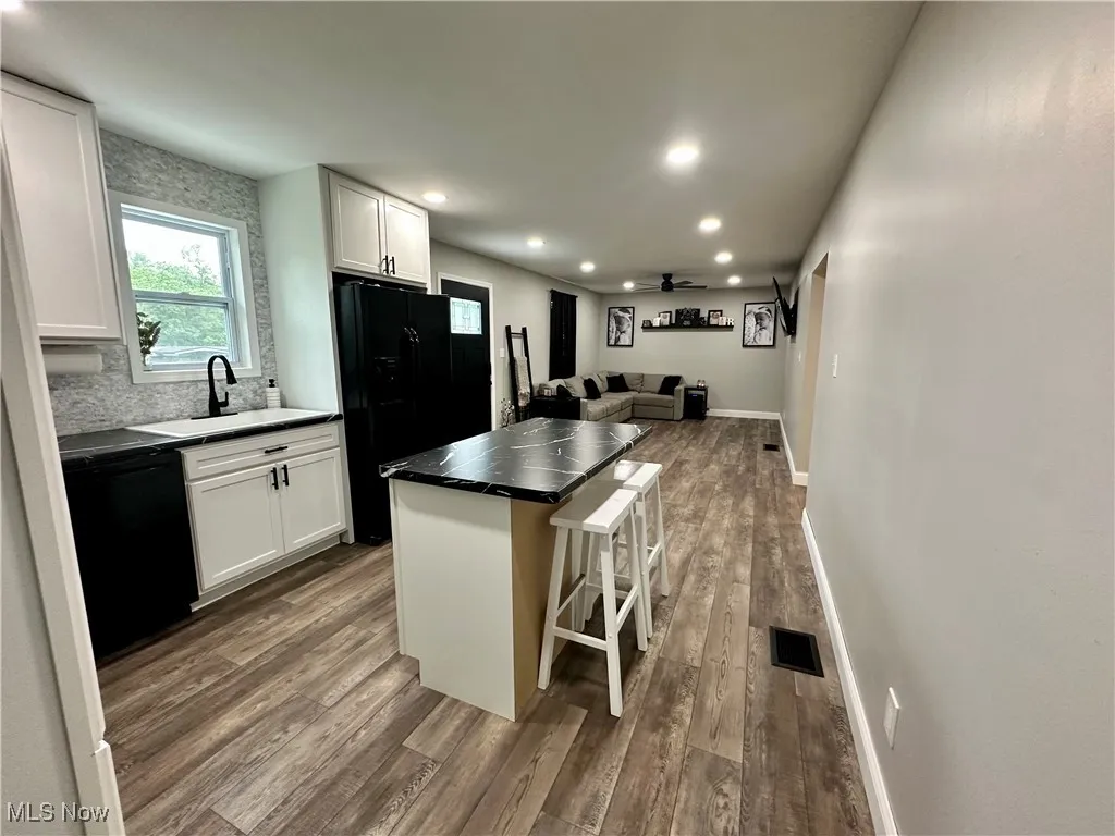 Kitchen featuring black appliances, open floor plan, dark wood-type flooring, a sink, and white cabinetry