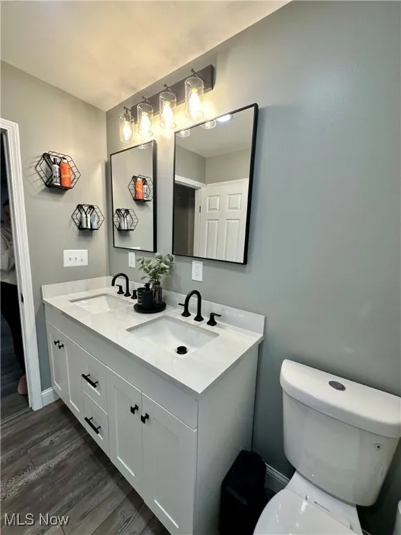 Bathroom with double vanity, toilet, and wood finished floors