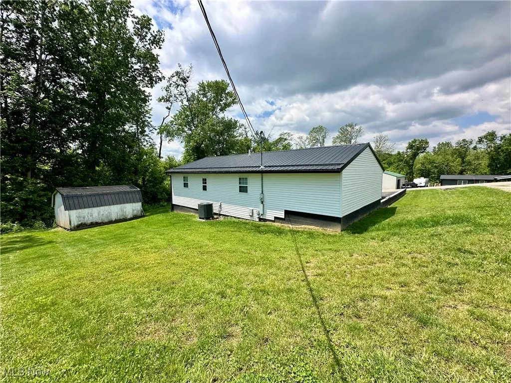 Rear view of house with central air condition unit and a lawn