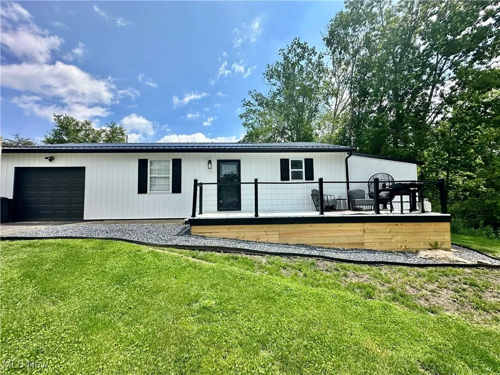 View of front facade with a garage, a front lawn, a wooden deck, and driveway