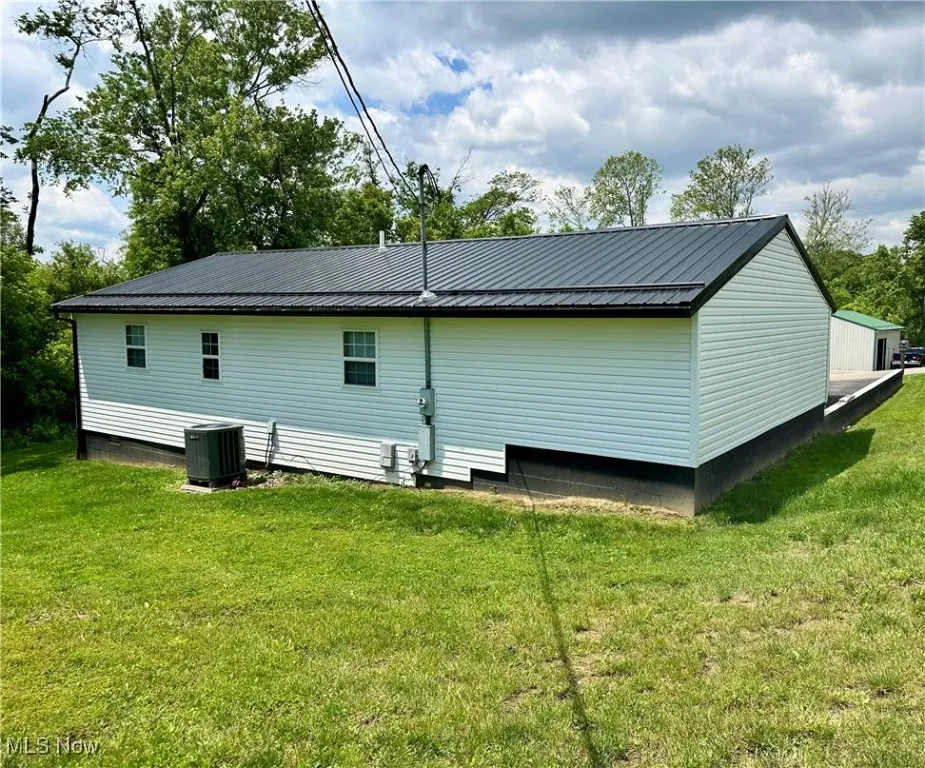Rear view of house with cooling unit, metal roof, and a yard