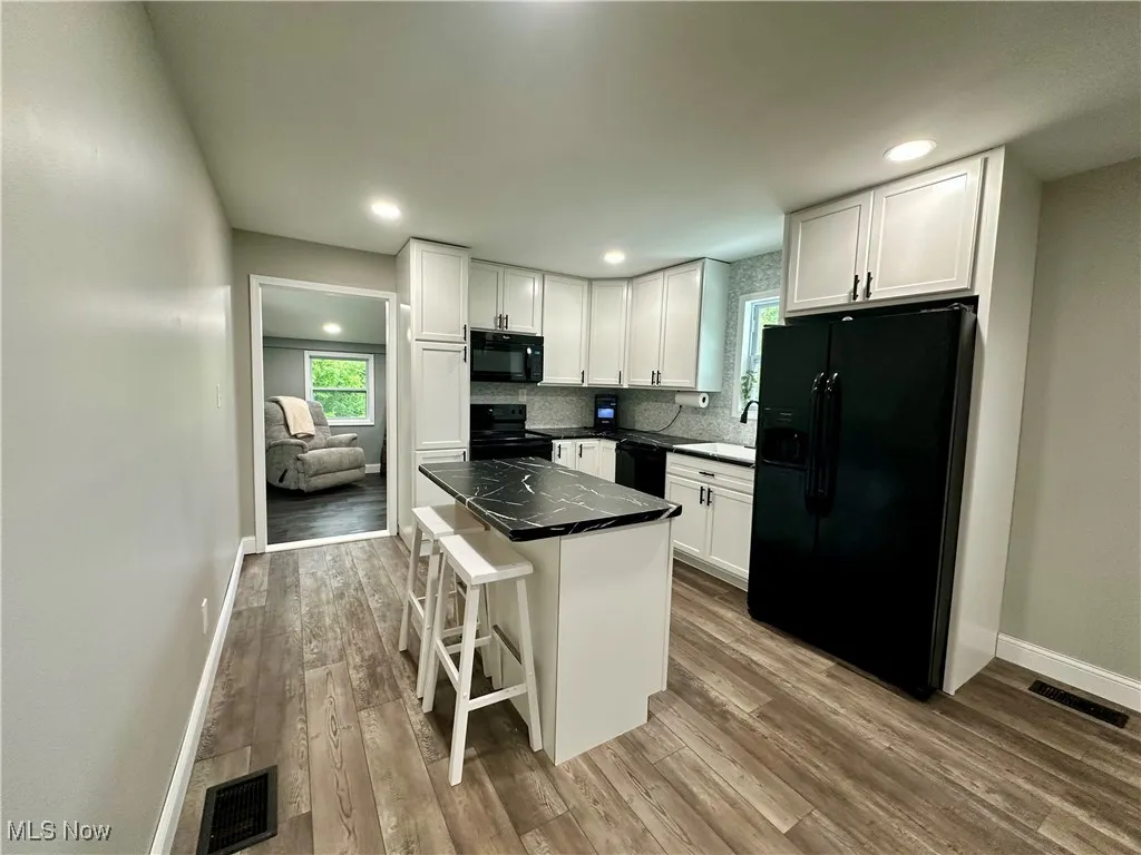 Kitchen with black appliances, white cabinetry, baseboards, a center island, and wood finished floors