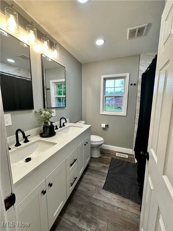 Full bathroom with double vanity, wood finished floors, toilet, healthy amount of natural light, and recessed lighting