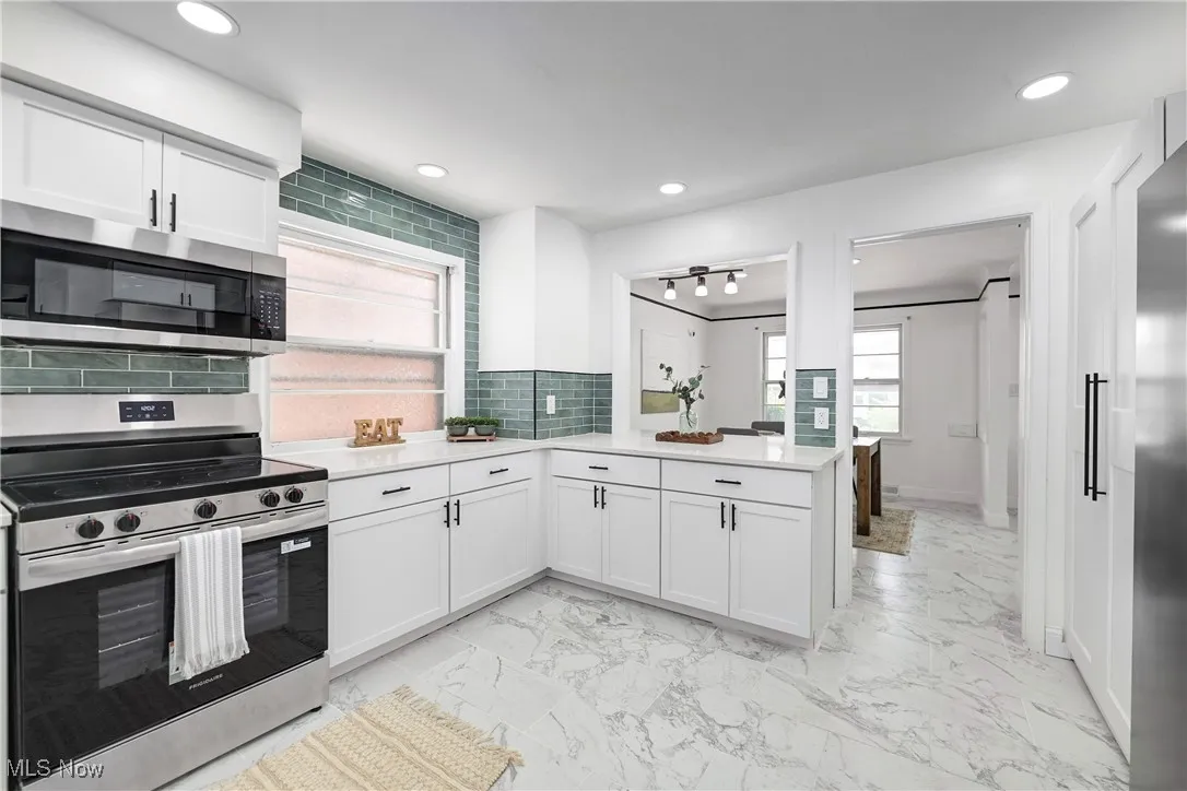 Kitchen featuring appliances with stainless steel finishes, light countertops, decorative backsplash, white cabinetry, and light marble finish flooring