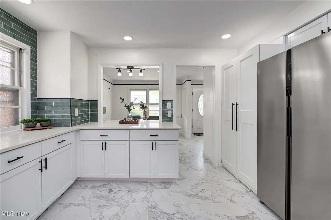Kitchen featuring refrigerator, light marble finish floors, recessed lighting, white cabinets, and backsplash