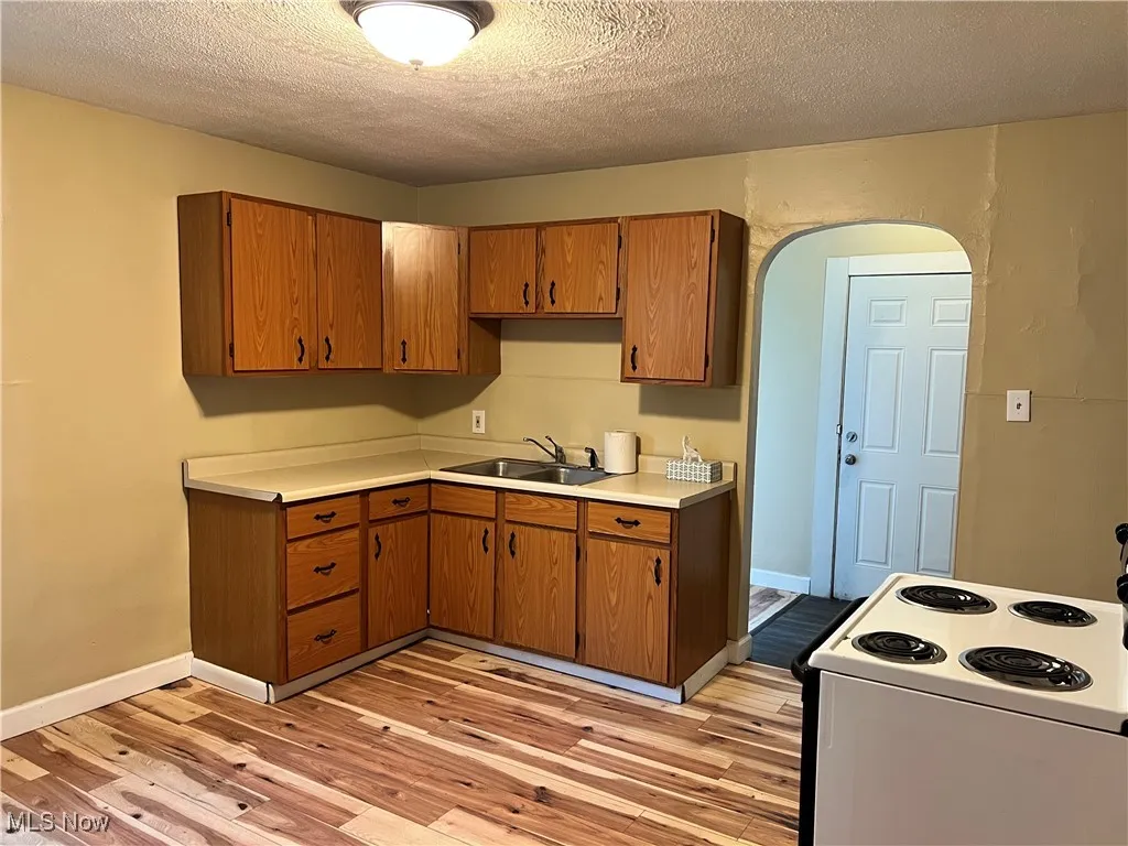 Kitchen with a sink, white range with electric cooktop, light wood finished floors, light countertops, and brown cabinetry