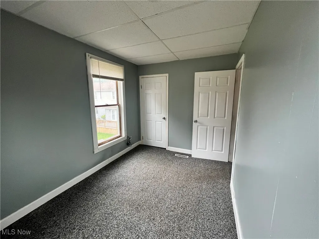 Unfurnished bedroom featuring a paneled ceiling, baseboards, and dark colored carpet