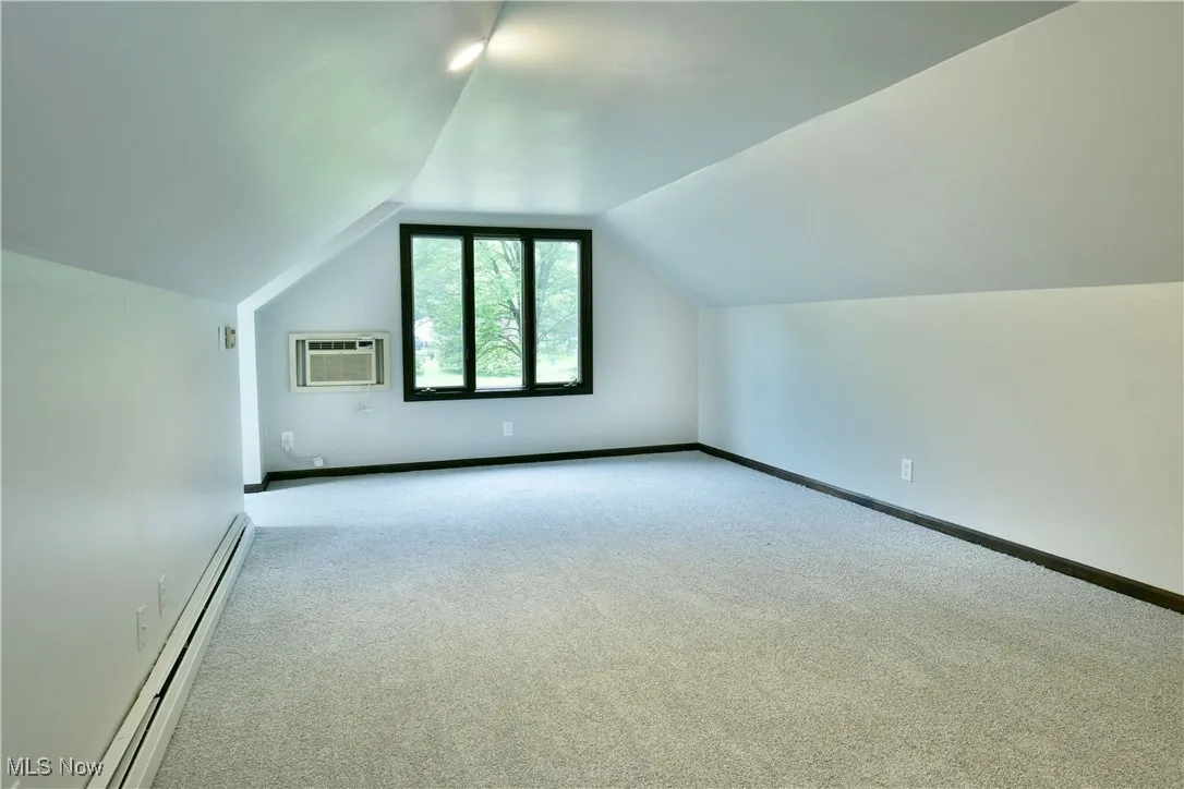 Additional living space with a baseboard heating unit, a wall mounted AC, carpet floors, vaulted ceiling, and baseboards