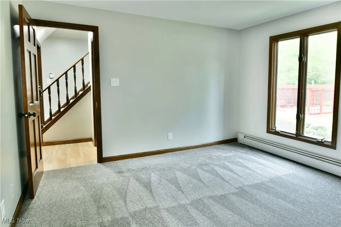 Empty room featuring carpet floors, plenty of natural light, baseboard heating, and baseboards