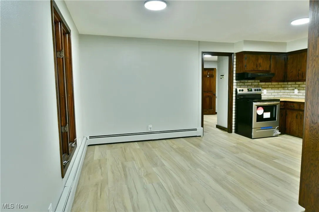 Kitchen with stainless steel electric range oven, under cabinet range hood, a baseboard heating unit, backsplash, and light wood-style floors