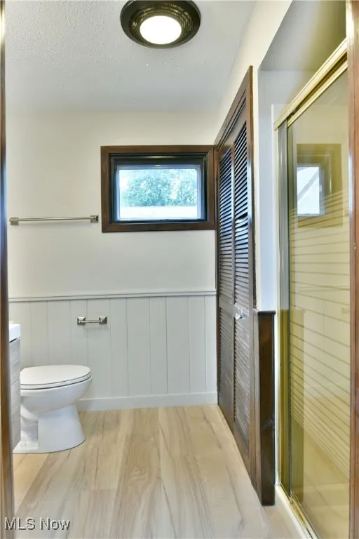 Bathroom with toilet, a shower stall, a wainscoted wall, and a textured ceiling