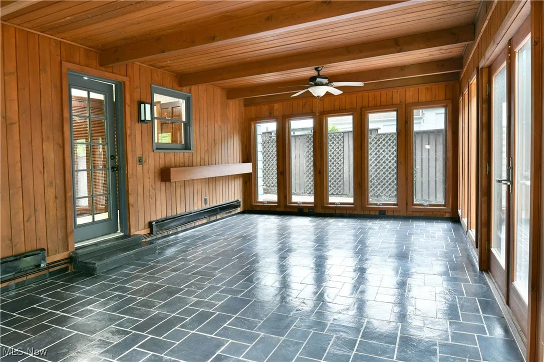 Unfurnished living room featuring a baseboard heating unit, plenty of natural light, ceiling fan, wood ceiling with exposed beams, and wood walls