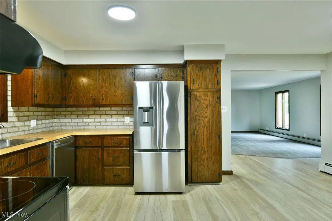 Kitchen with stainless steel appliances, baseboard heating, a sink, tasteful backsplash, and light countertops