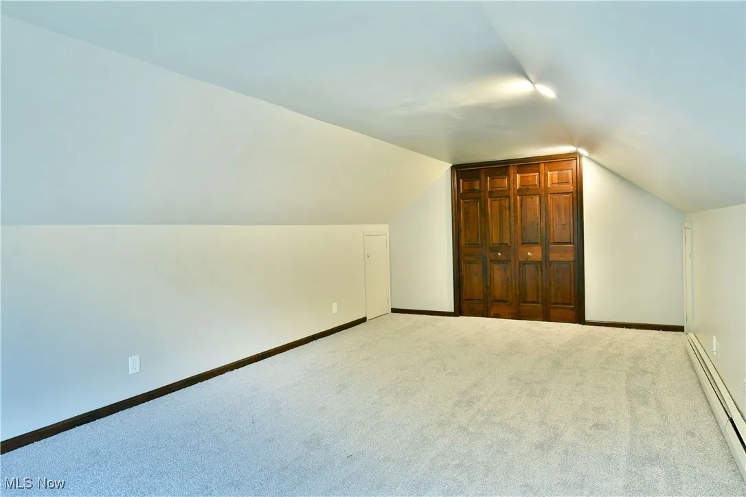 Additional living space with a baseboard radiator, vaulted ceiling, carpet flooring, and baseboards