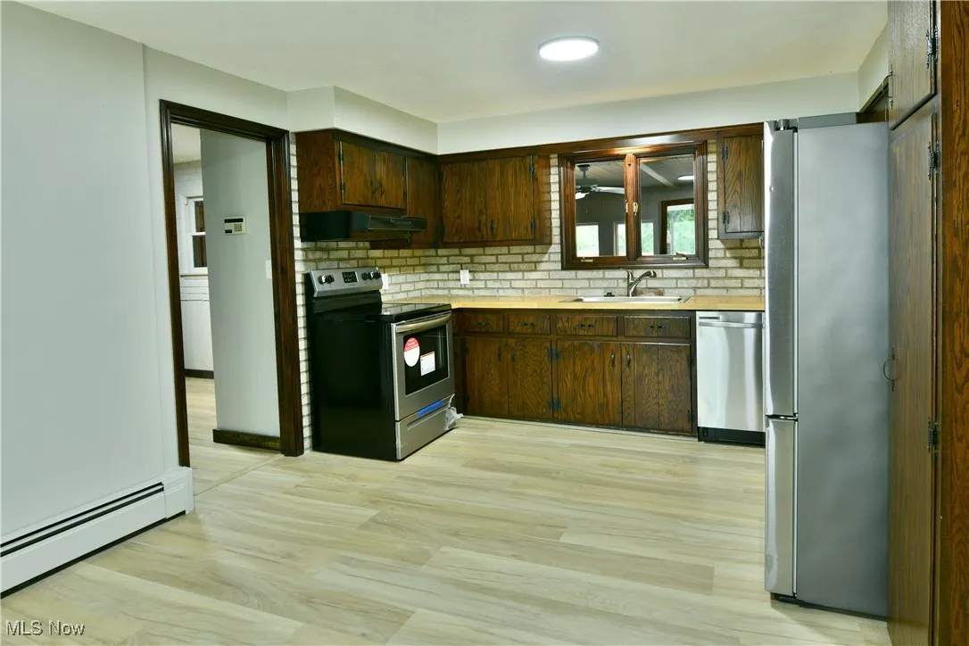 Kitchen featuring appliances with stainless steel finishes, a sink, under cabinet range hood, light countertops, and backsplash