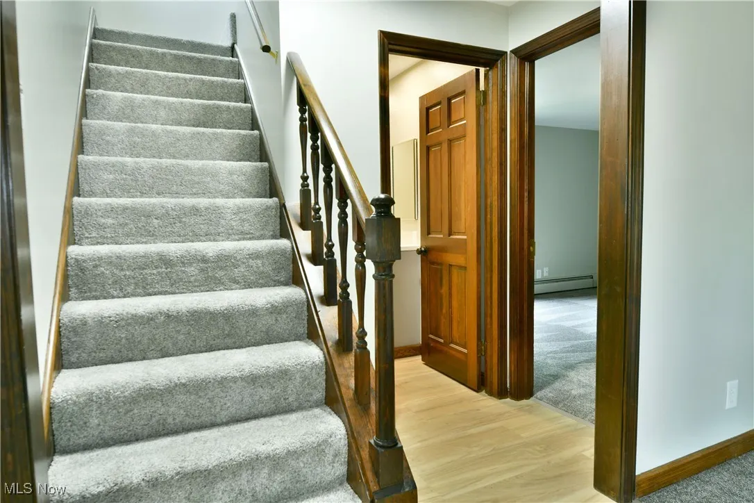 Stairs featuring a baseboard heating unit, wood finished floors, and baseboards