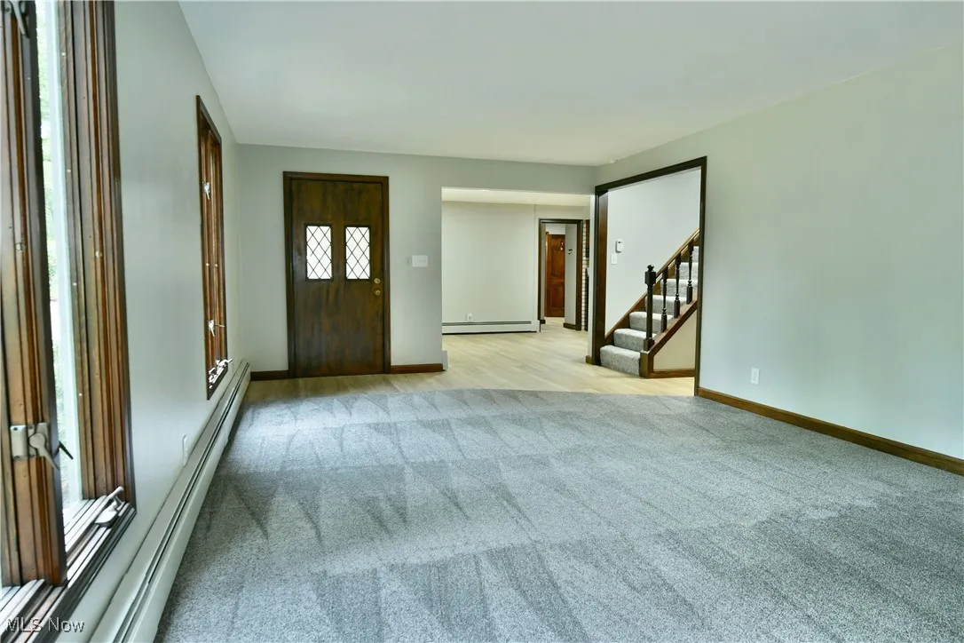 Entryway featuring light colored carpet, a baseboard heating unit, stairway, a baseboard radiator, and baseboards
