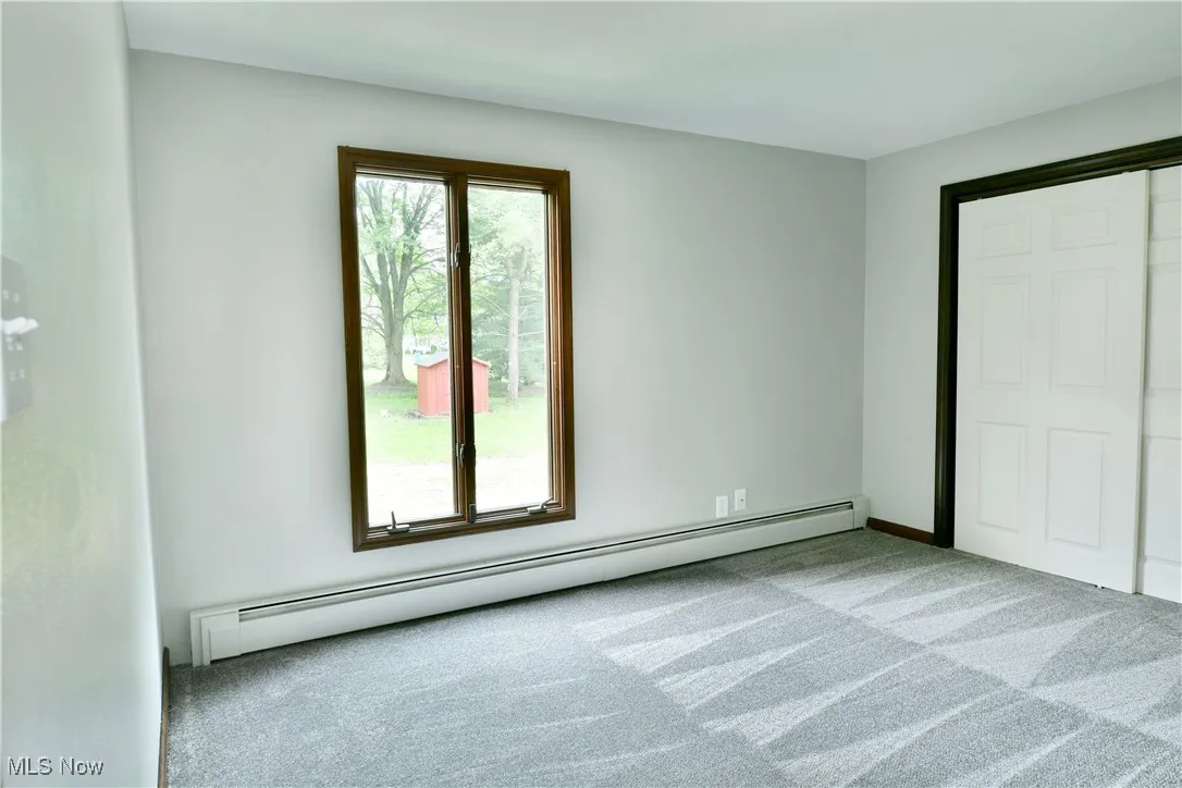 Unfurnished bedroom with a baseboard heating unit and carpet flooring