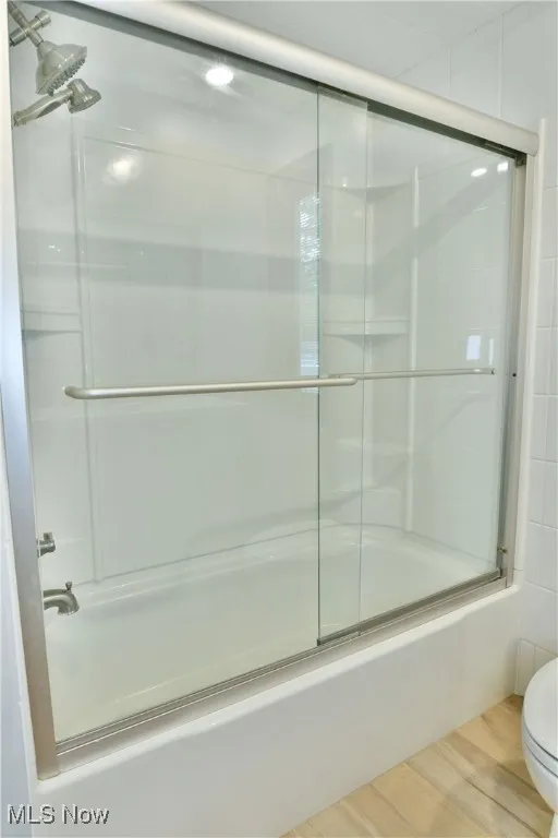 Bathroom with bath / shower combo with glass door, toilet, and wood finished floors