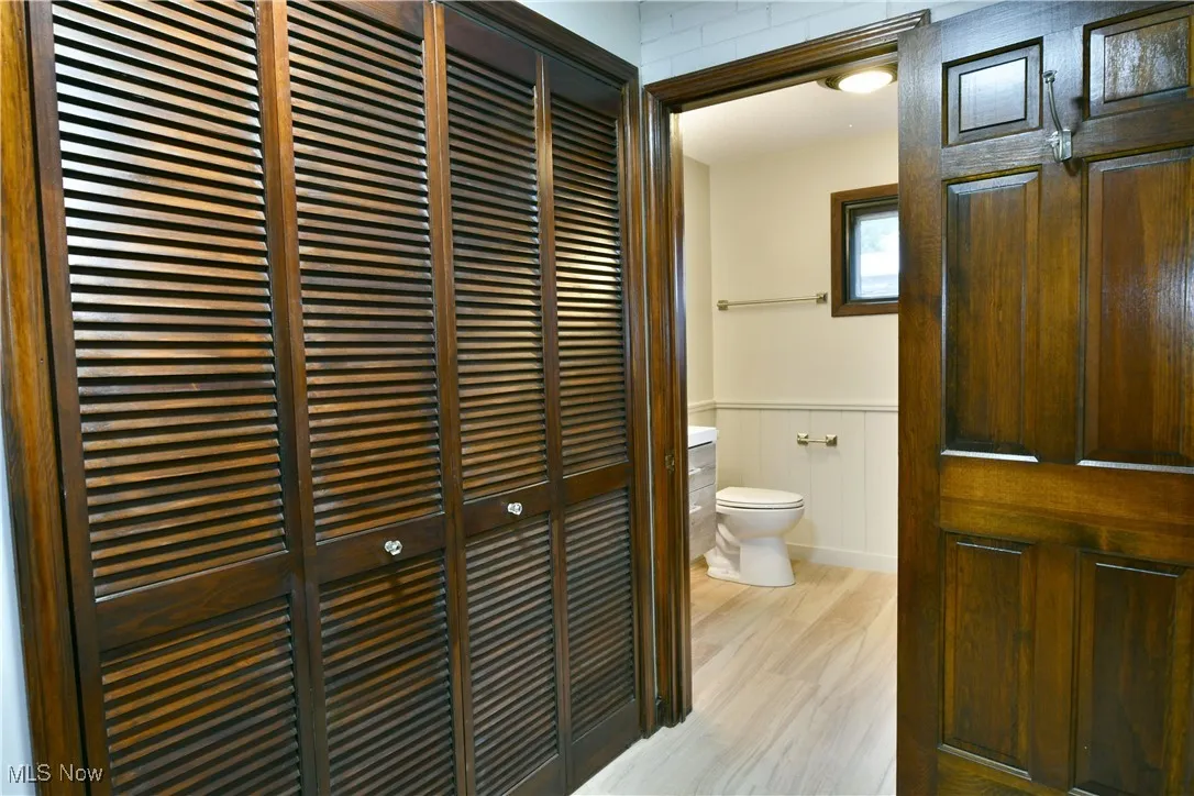 Bathroom featuring toilet, wood finished floors, wainscoting, and a closet