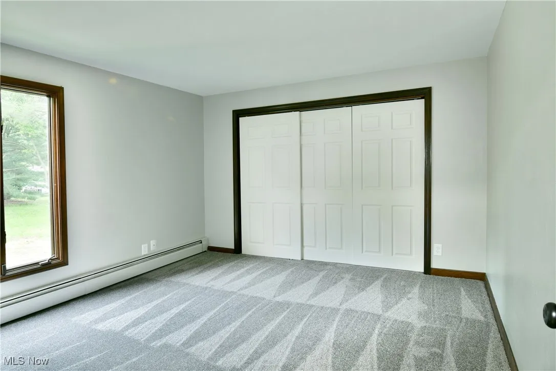 Unfurnished bedroom featuring a baseboard radiator, carpet floors, a closet, and baseboards