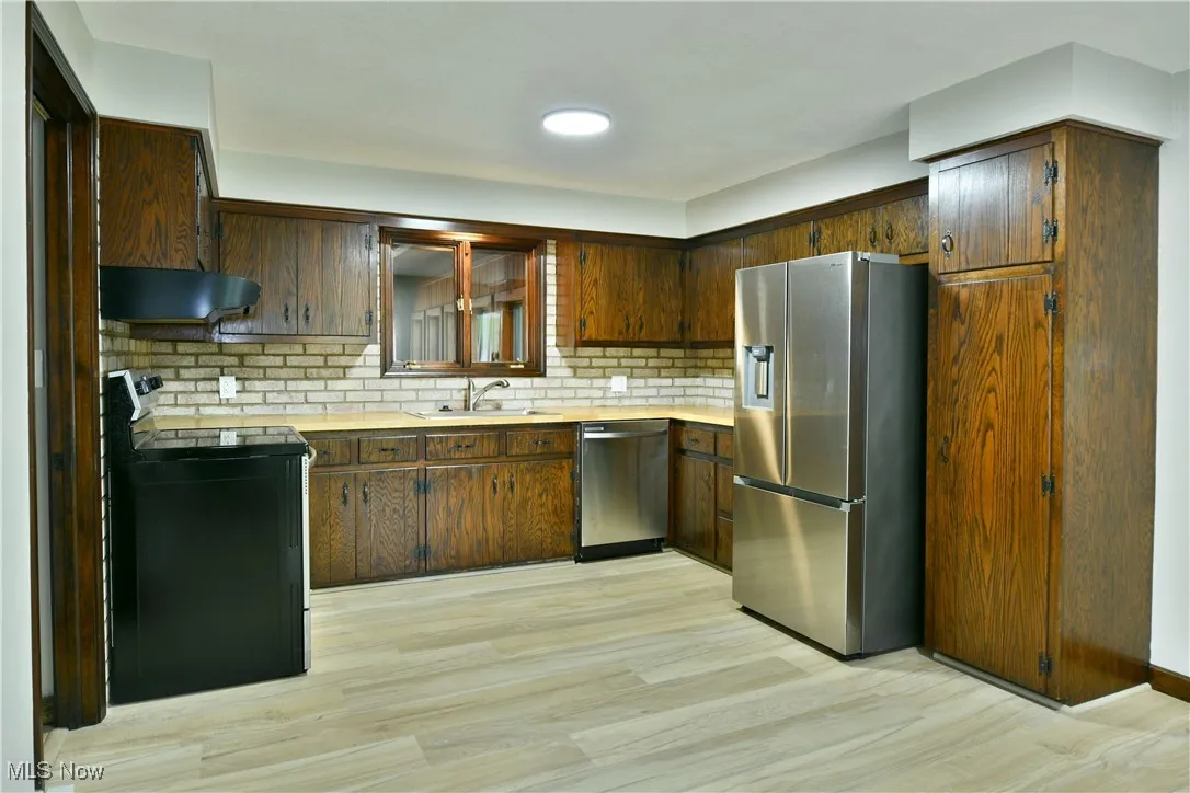 Kitchen featuring appliances with stainless steel finishes, a sink, under cabinet range hood, and light countertops