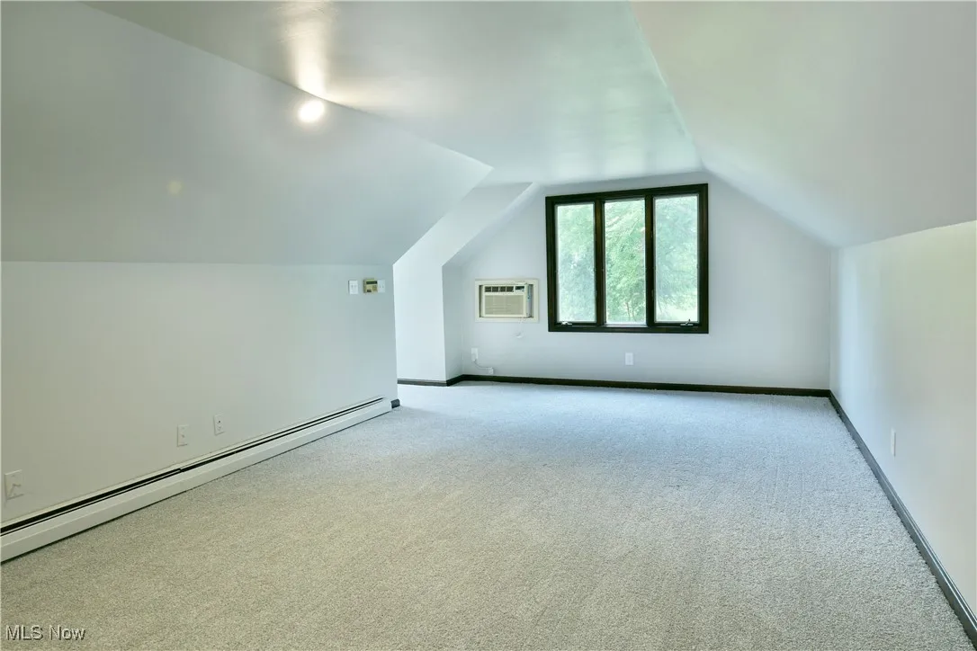 Additional living space with a baseboard heating unit, a wall mounted AC, carpet flooring, and vaulted​​‌​​​​‌​​‌‌​‌‌​​​‌‌​‌​‌​‌​​​‌​​ ceiling