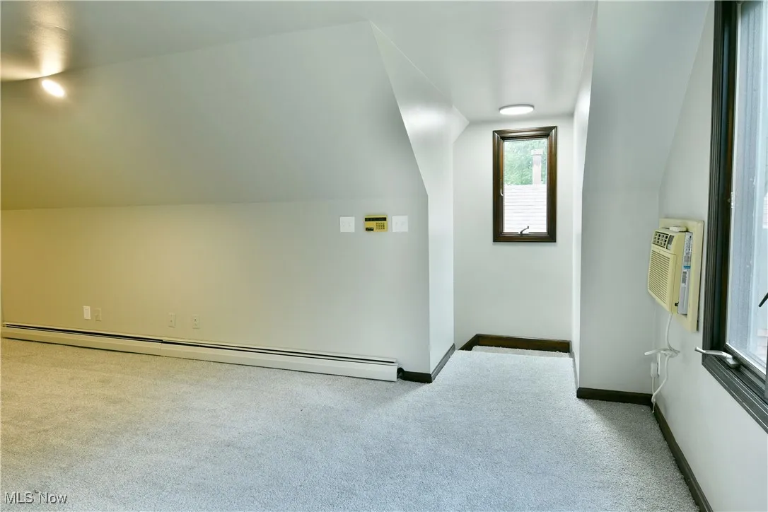 Bonus room with carpet, lofted ceiling, a baseboard heating unit, baseboards, and an AC wall unit