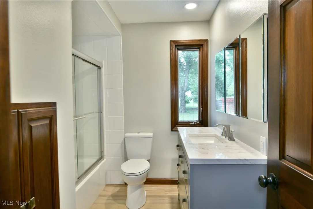 Bathroom with toilet, vanity, enclosed tub / shower combo, wood finished floors, and baseboards