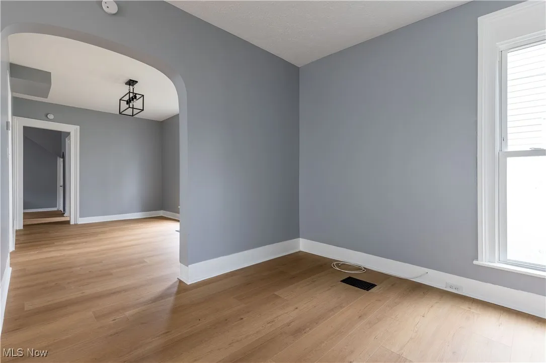 Unfurnished room with arched walkways, light wood-type flooring, healthy amount of natural light, and baseboards