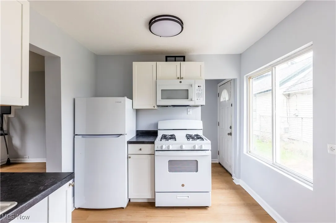 Kitchen featuring white appliances, plenty of natural light, light wood-type flooring, and dark countertops