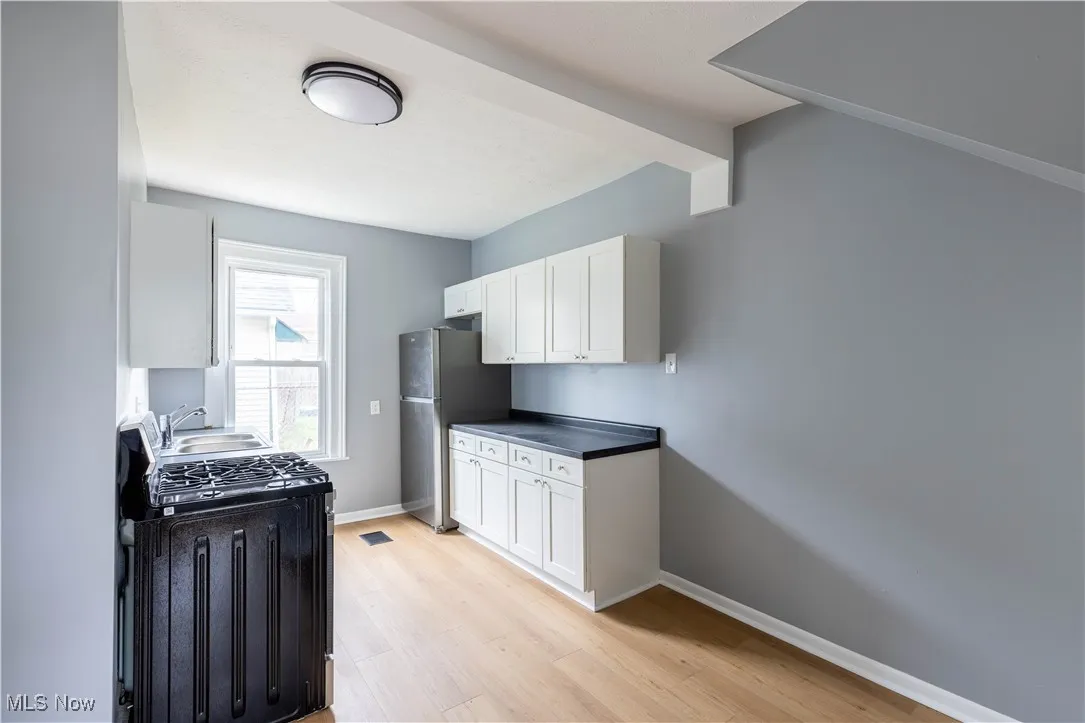 Kitchen with freestanding refrigerator, a sink, light wood-style flooring, and white cabinetry