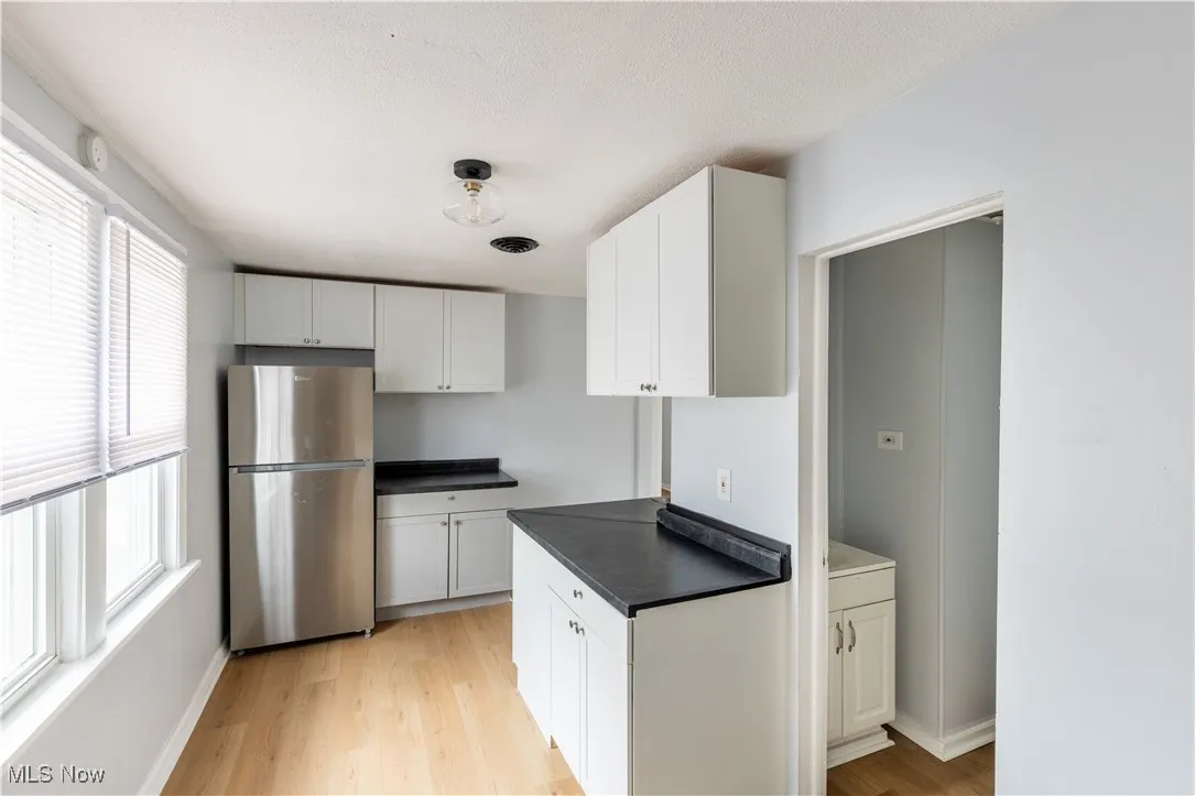 Kitchen with freestanding refrigerator, dark countertops, light wood-style flooring, and white​​‌​​​​‌​​‌‌​‌‌​​​‌‌​‌​‌​‌​​​‌​​ cabinets