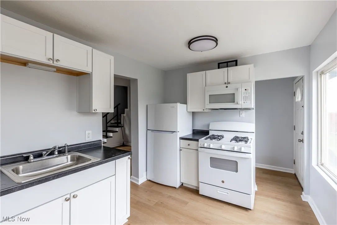 Kitchen featuring white appliances, a sink, dark countertops, and light wood-style flooring